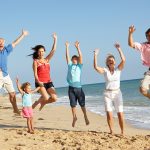 Portrait-Of-Three-Generation-Family-On-Beach-Holiday-Jumping-In-Air